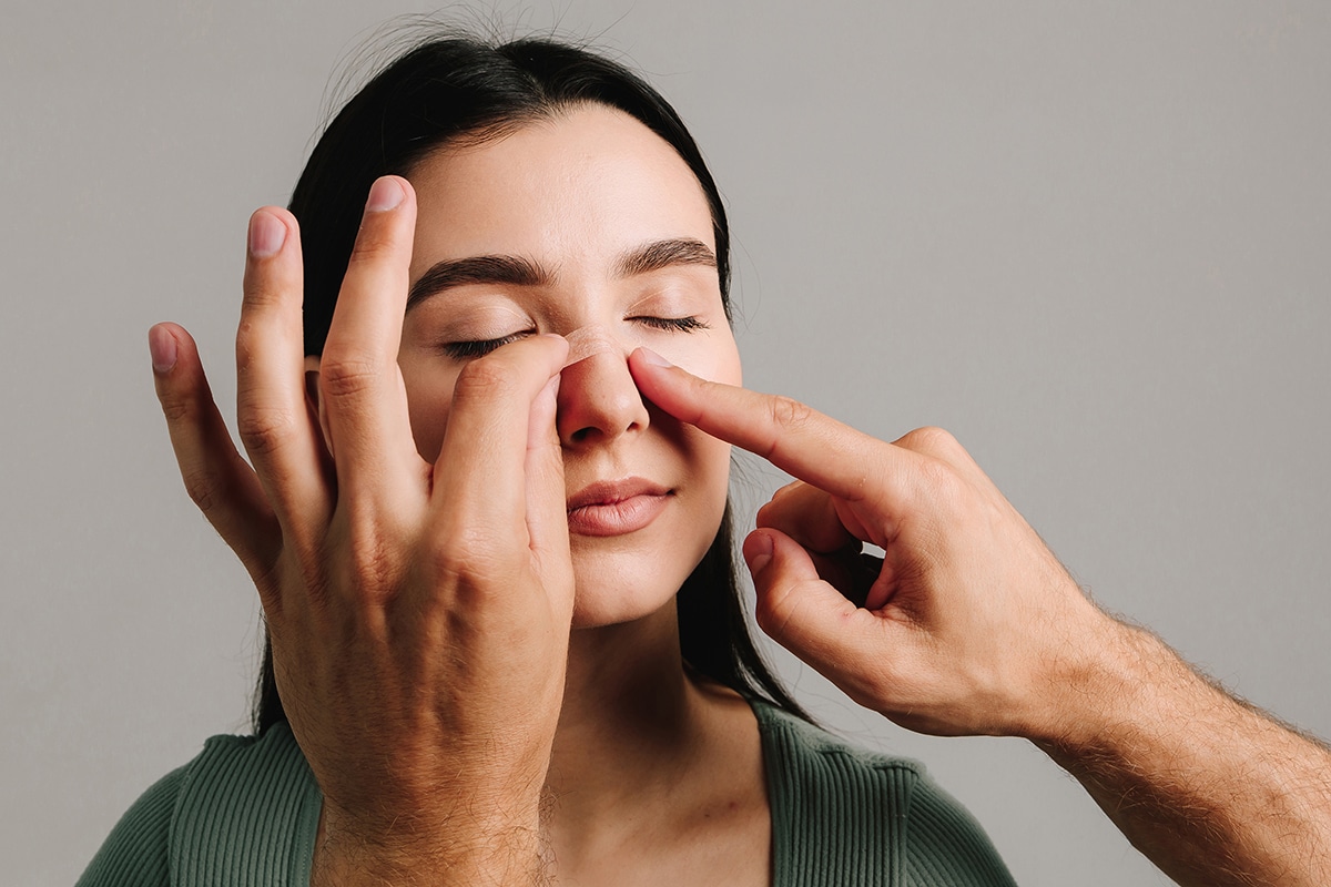 Woman with eyes closed as hands apply a nasal strip to her nose. Woman with eyes closed as hands apply a nasal strip to her nose.