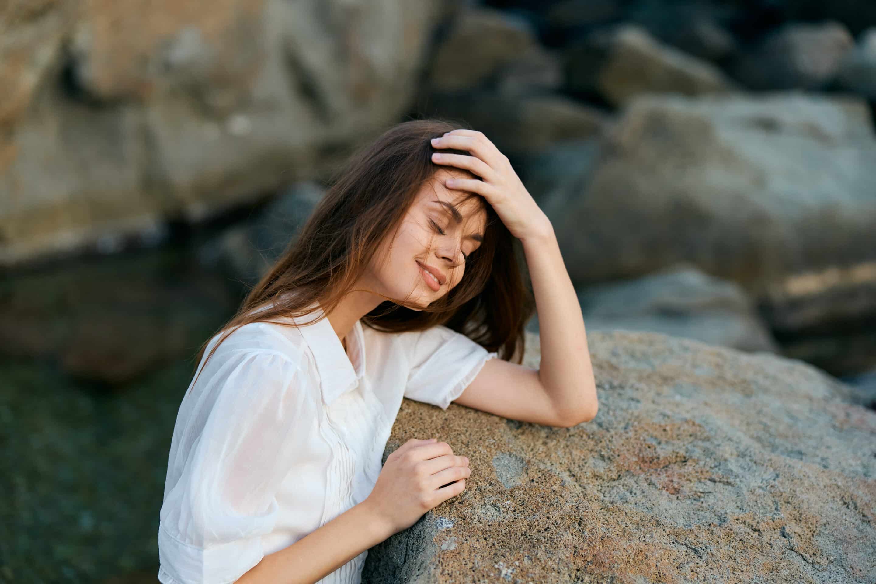 Serene woman sitting on ocean rock with hands on head, gazing at camera in peaceful contemplation Kenalog Injections for healing process