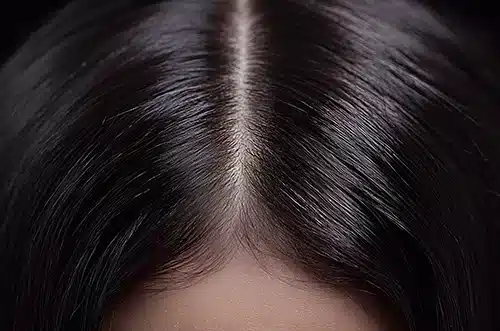 Overhead macro shot of a straight center part in clean, dark brown hair showcasing a healthy scalp.